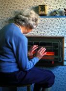 A693C0 elderly lady holding her hands near an electric fire